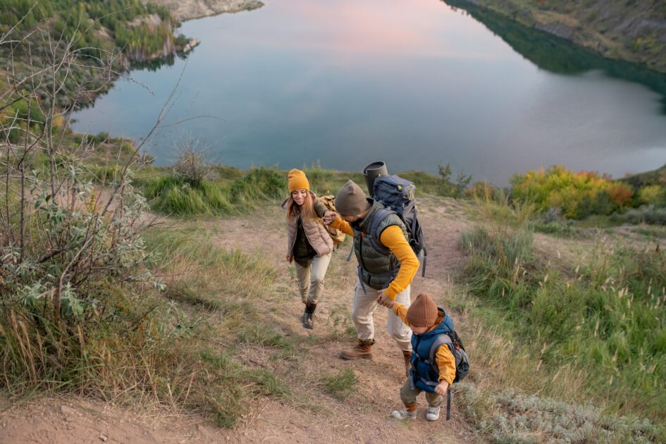 Family of hikers with backpacks climbing mountain against river during trip